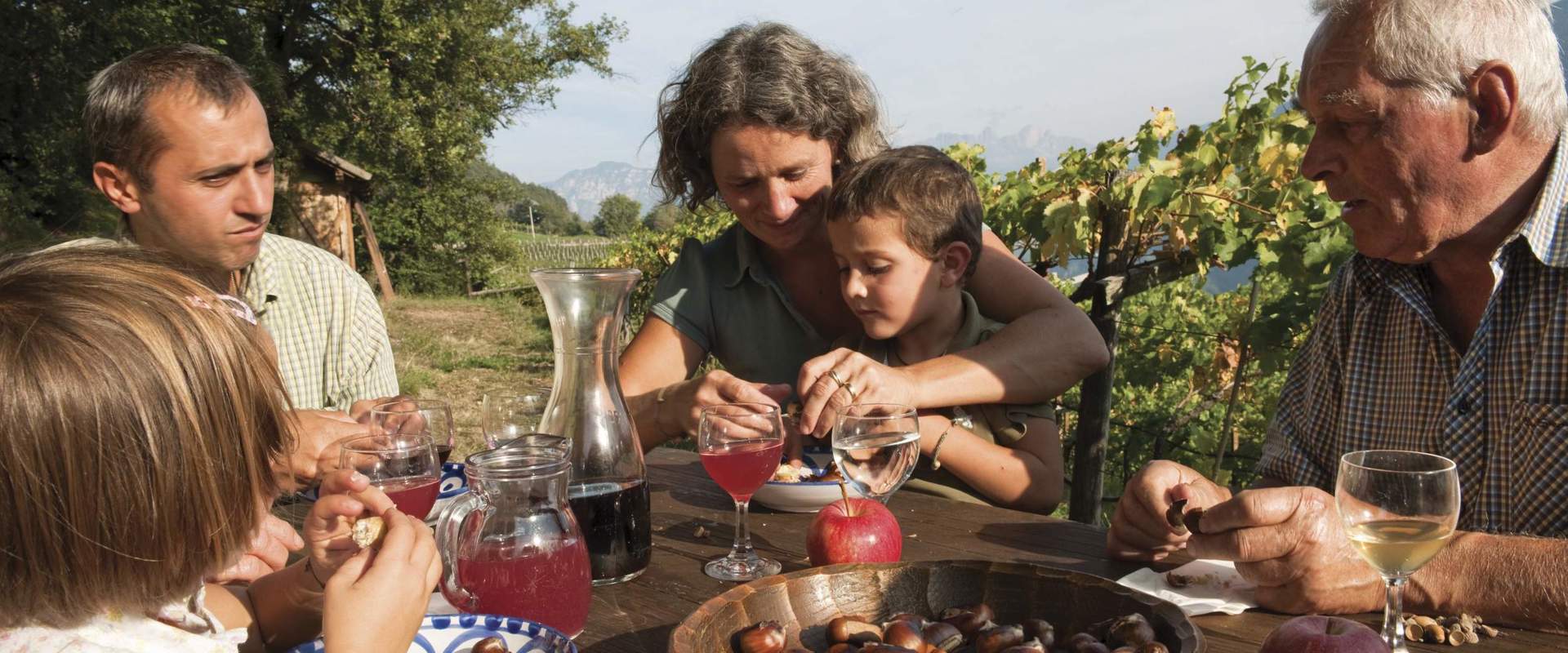 Großfamilie sitzt im Freien am Tisch, isst Kastanien und trinkt Most.