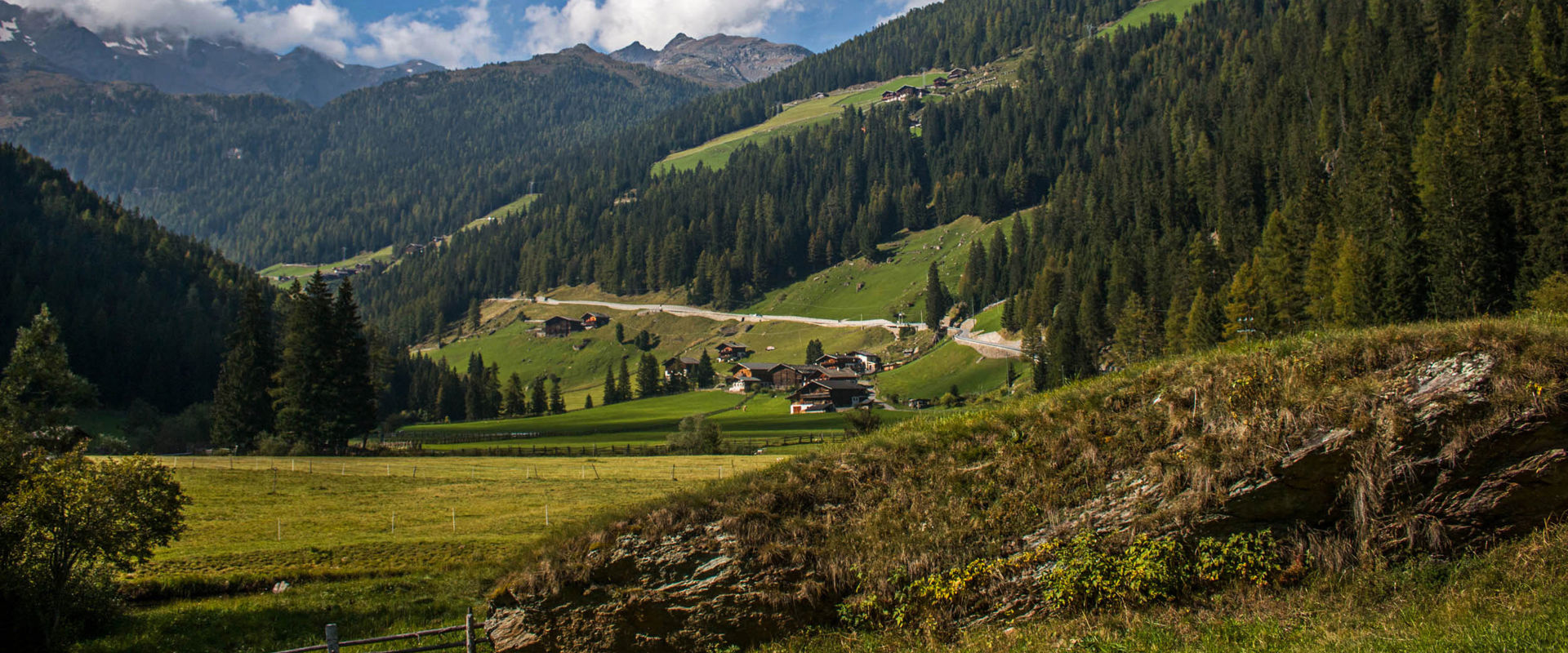 Ultental Berglandschaft mit bewaldeten Hängen, Straße und verstreut liegenden Häusern.