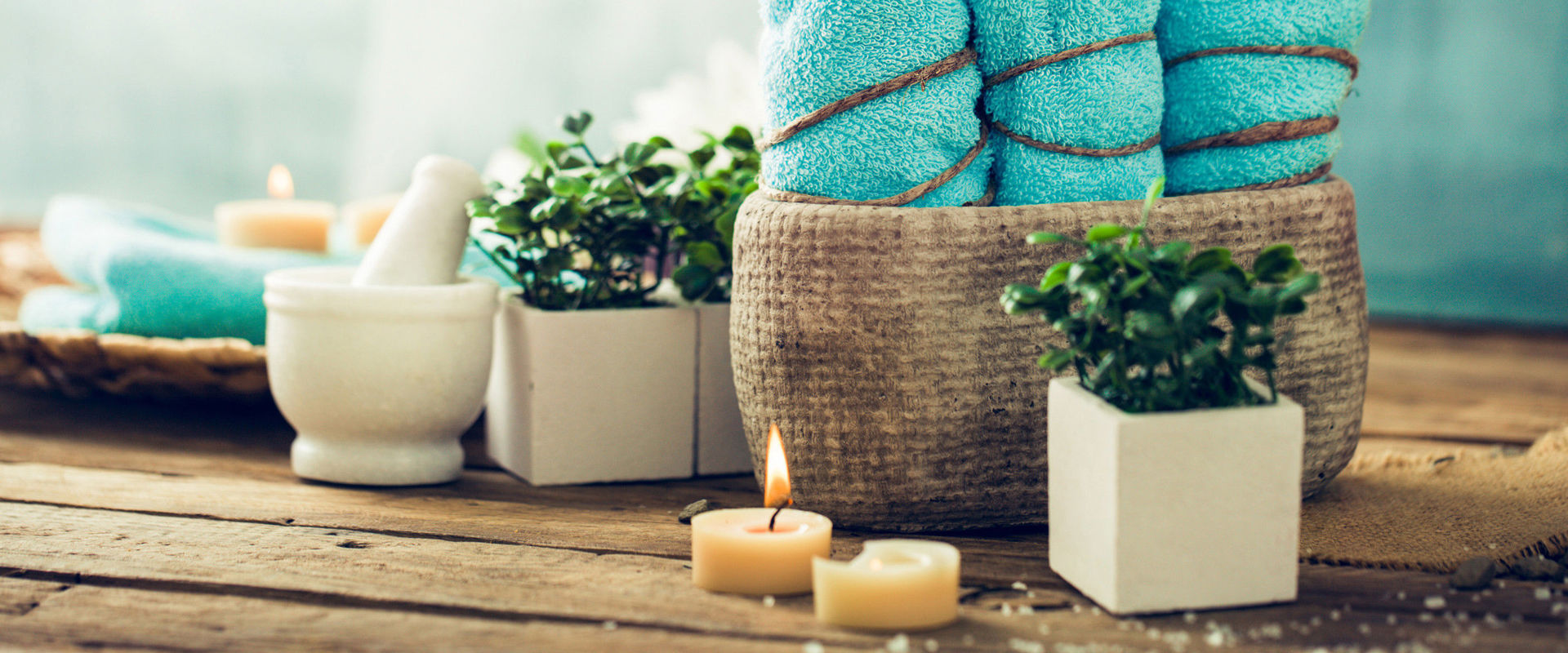 Wellnessprodukte 3 türkise Handtücher, Kerzen und Blumen stehen auf einer Holzunterlage.