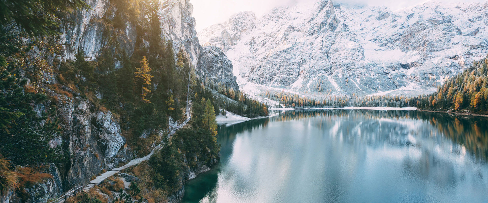 Bergsee im Winter Tiefblauer Bergsee, umgeben von schneebedeckten Bergen und Wäldern. Links im Bild startet ein schmaler Pfad um den See herum.