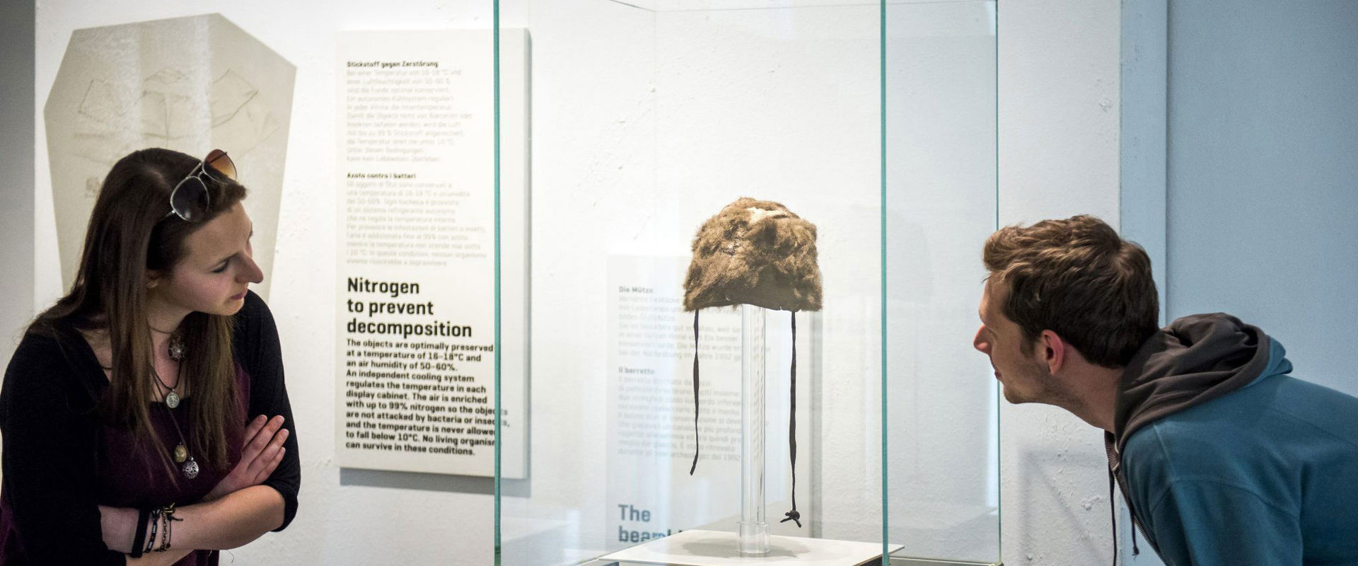 Südtiroler Archäologiemuseum 2 Besucher bewundern eine alte Mütze in einer Vitrine.