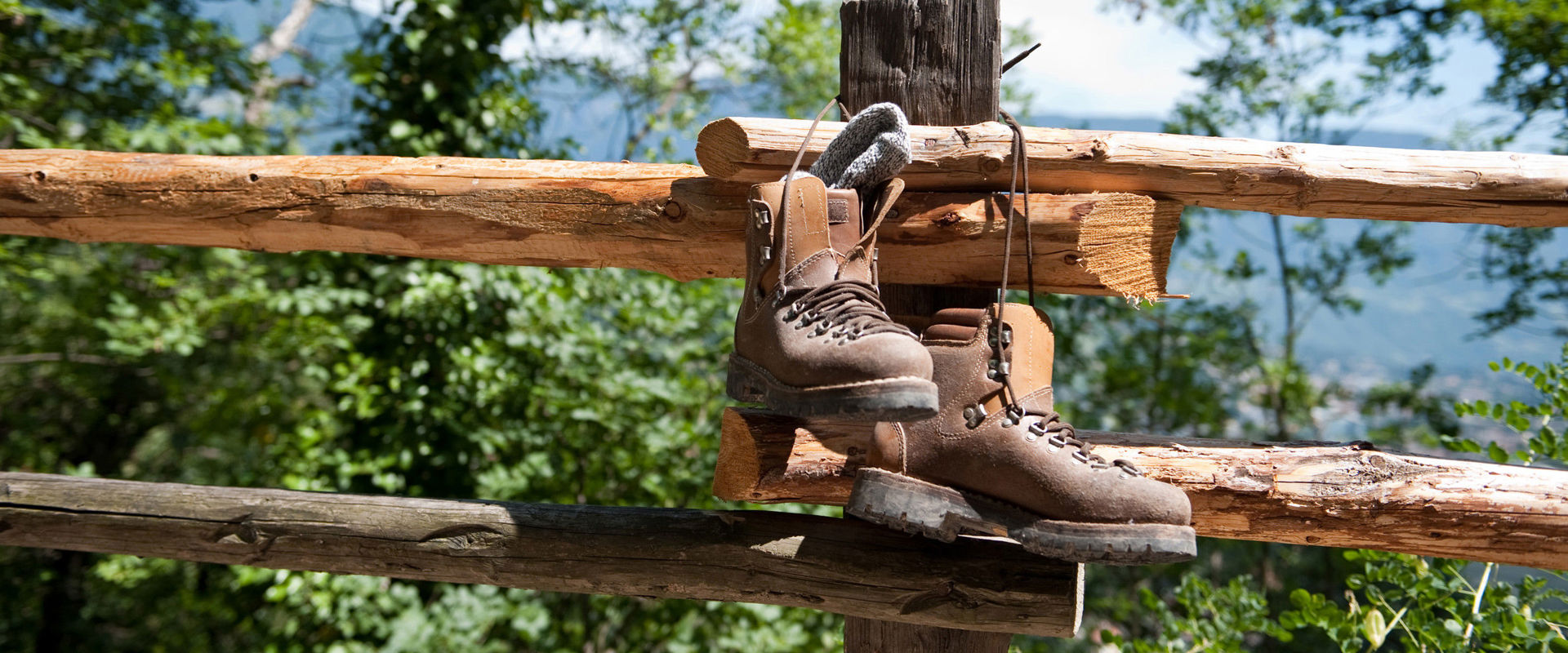 Ausrüstung für Sommerausflüge am Berg Ein Paar Bergstiefel hängen an einem sonnigen Tag an einem Holzzaun.