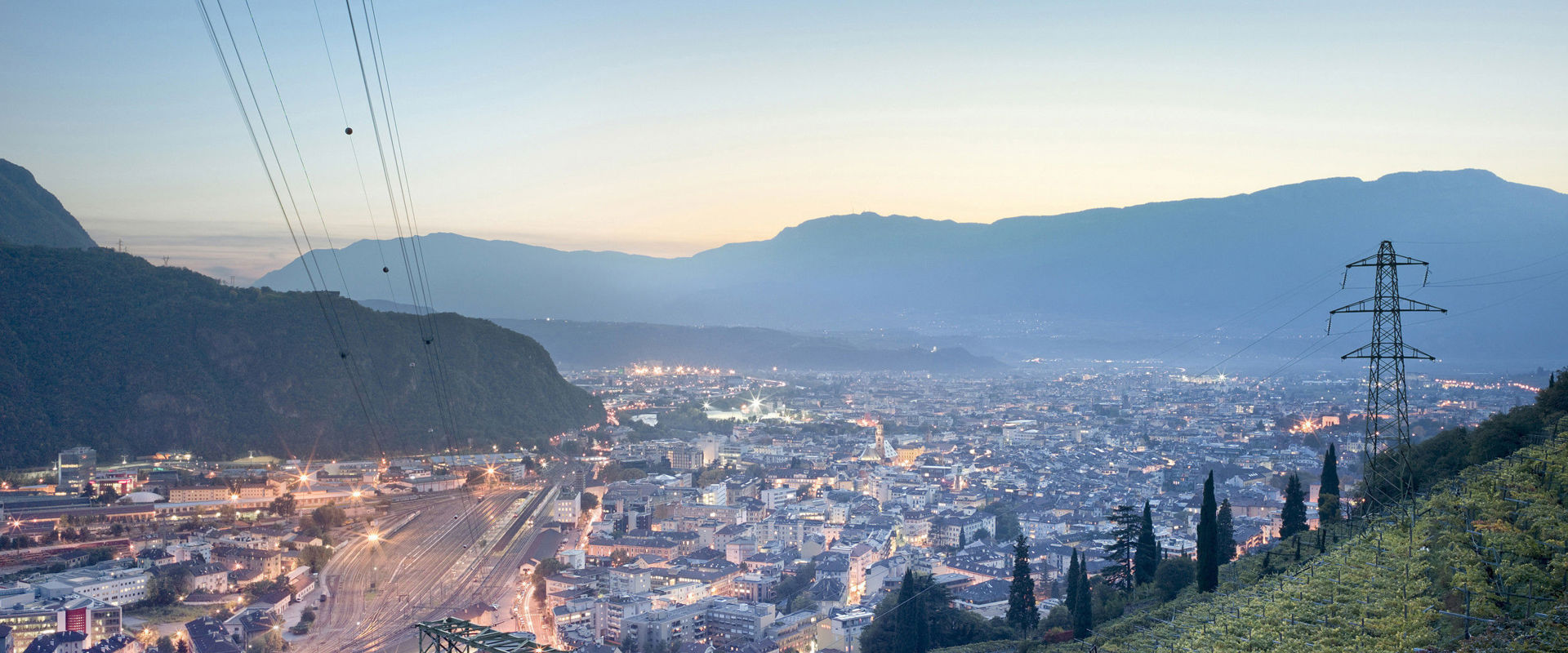 Frühabendlich beleuchtete Stadt, gesäumt von Weingärten.