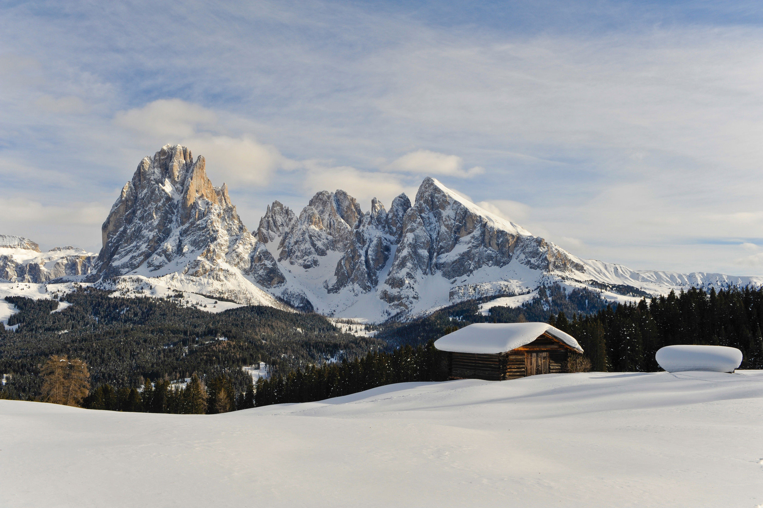 Winterpanorama mit schneebedeckter Holzhütte und weißen Bergspitzen.