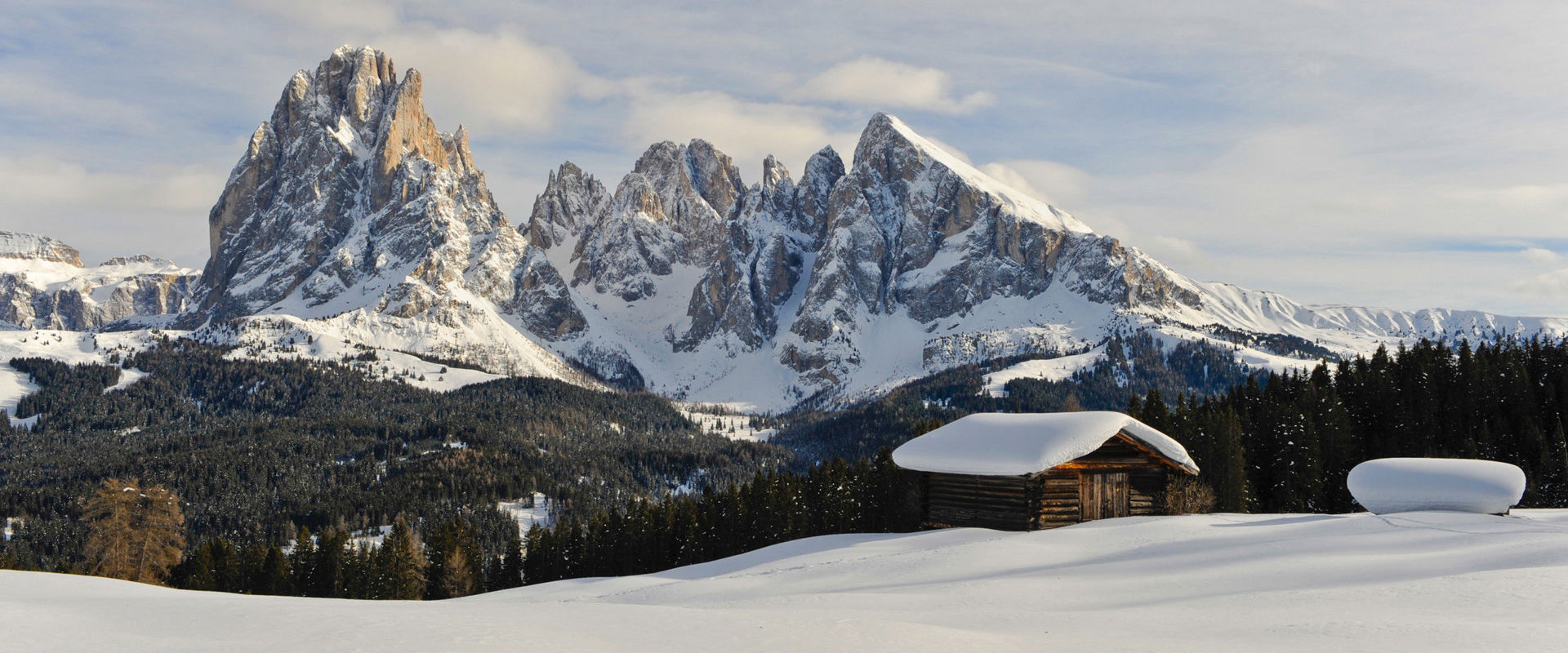 Winter auf der Seiser Alm Winterpanorama mit schneebedeckter Holzhütte und weißen Bergspitzen.