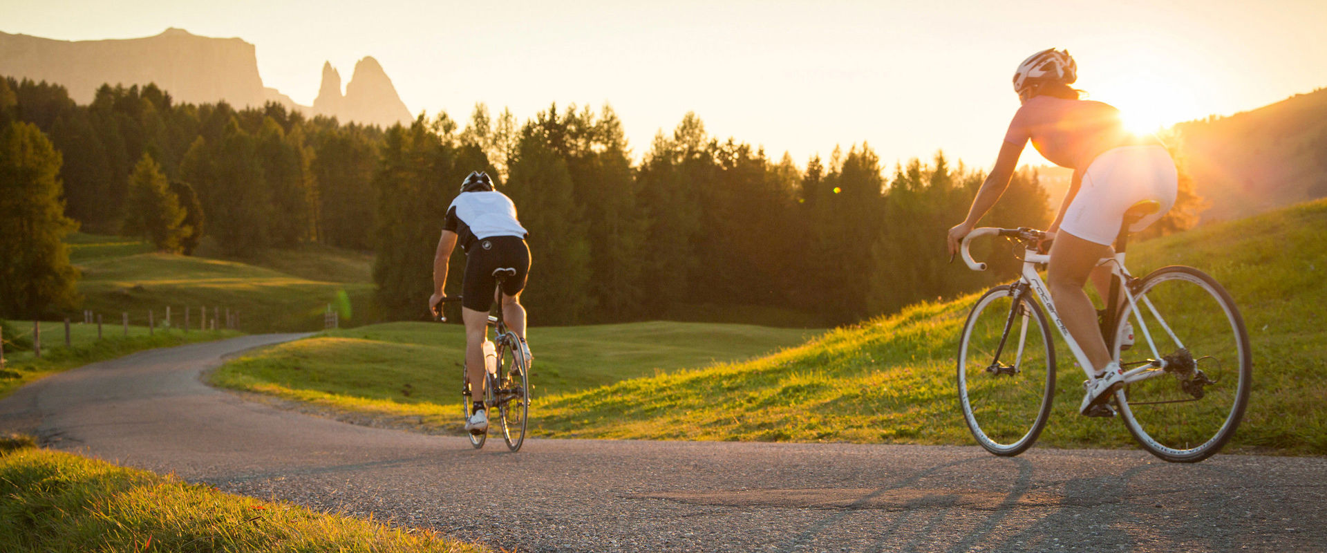 Rennrad fahren am Berg. 2 Radfahrer fahren bei einem atemberaubenden Sonnenuntergang den Berg hinab.