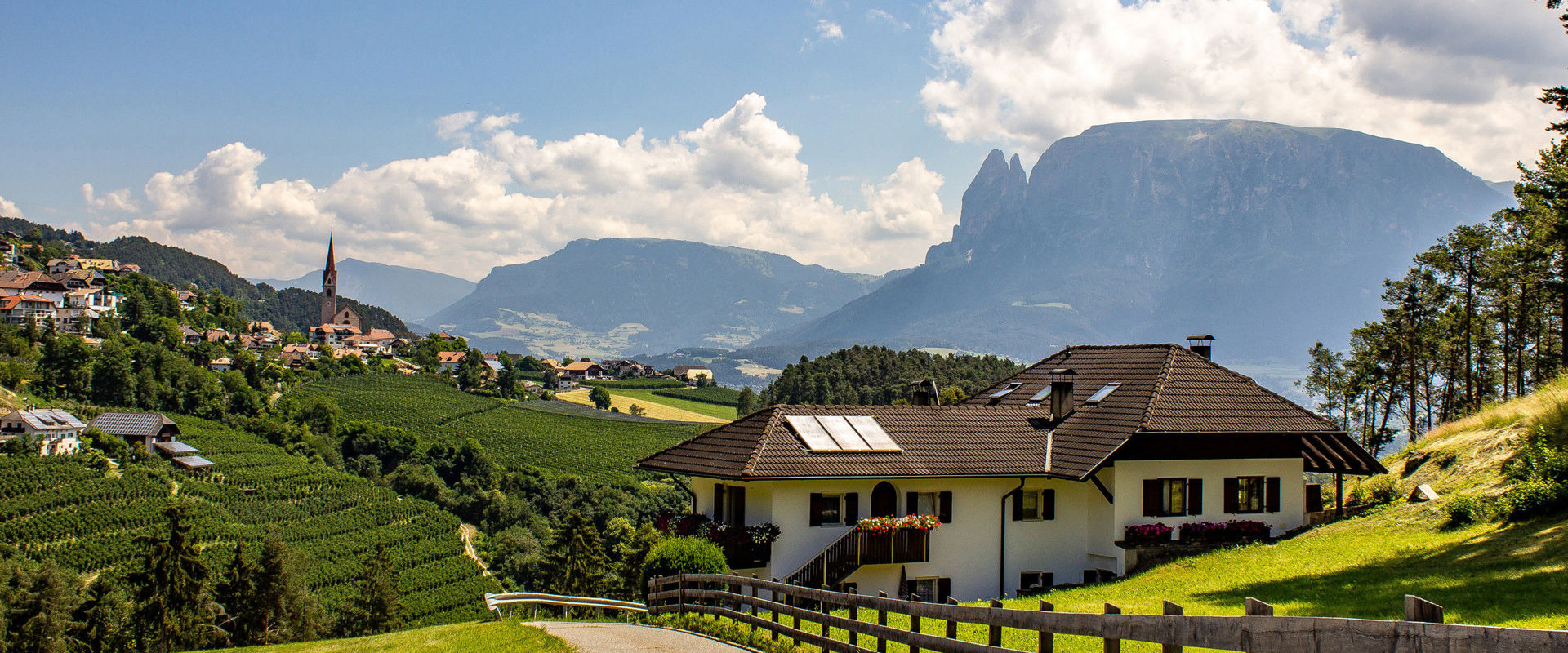 Ritten Straße mit Haus am Ritten, an Wiesen und Weinbergen mit Kirche und Schlern im Hintergrund