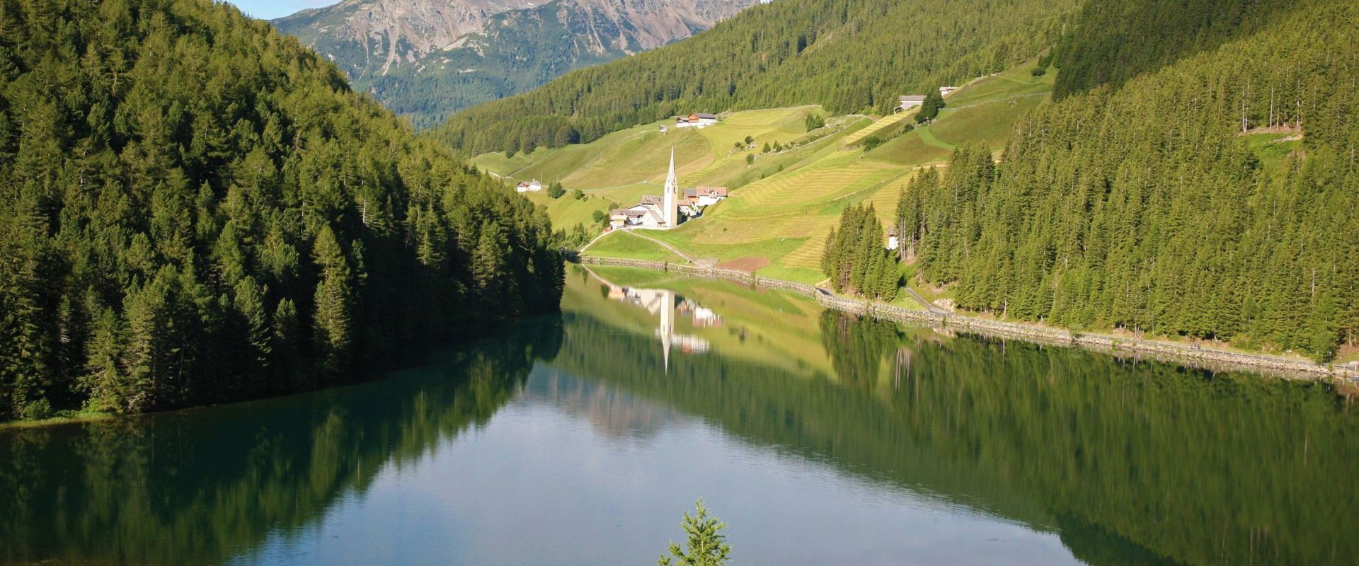Idyllisch liegender Durnholzer See mit Bergpanorama und Blick auf einer kleinen Kirche.