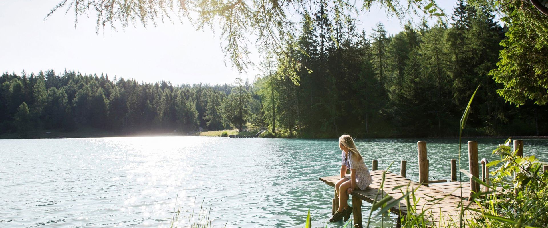 Junges Mädchen mit blondem Haar sitzt auf dem Steg, am Ufer des Sees.