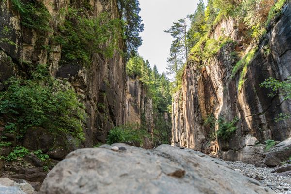Links und rechts vom Bild sieht man rötliche, steil nach oben gehende Felswände, die mit einigen Bäumen bewachsen sind.