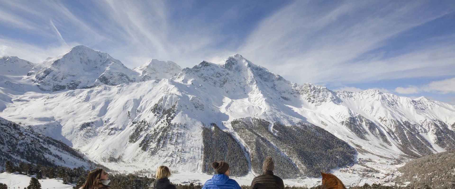 Nationalpark Stilfserjoch im Winter Gruppe junger Mädchen mit Hund sitzt am Berggipfel im Schnee und bewundert die Bergspitzen.