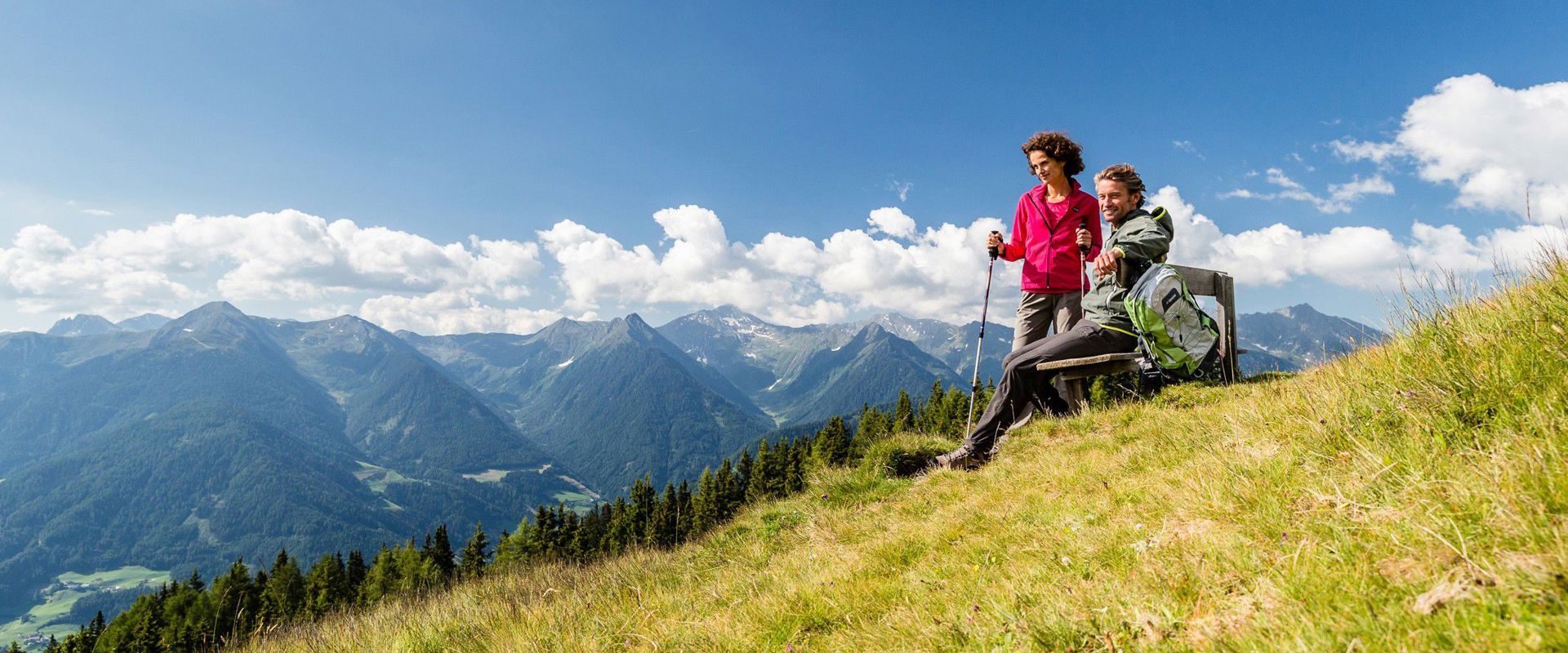 Zwei Wanderer rasten auf einer Bank entlang des Weges, der zum Rosskopf in Sterzing führt.
