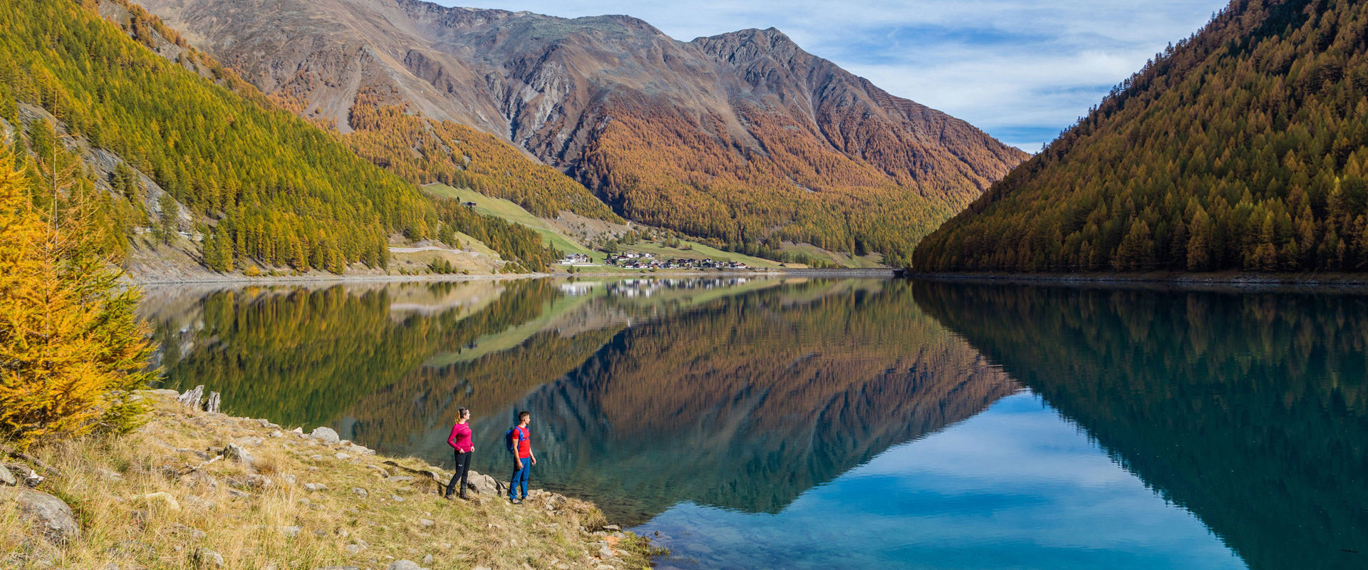 Junges Paar steht am Vernagt Stausee. Im Wasser spiegeln sich die umliegenden Berge.