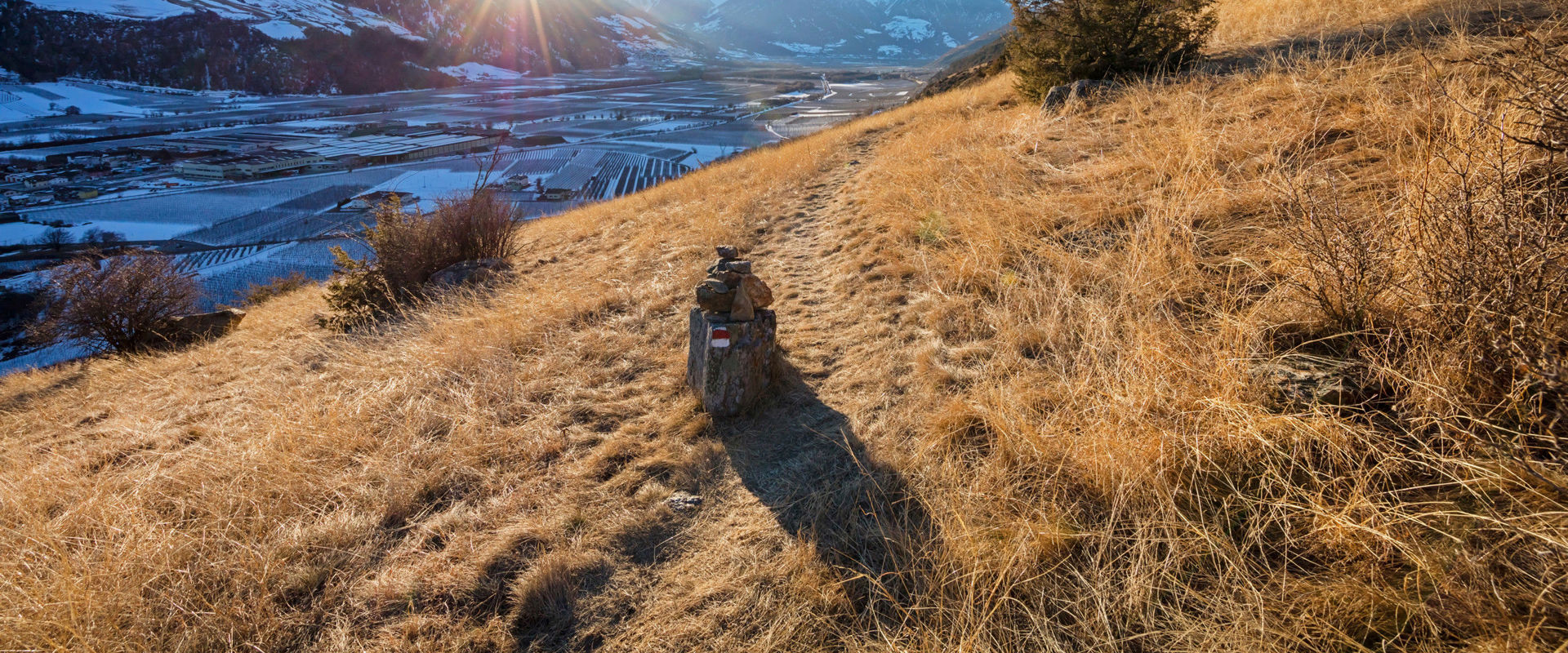 Vinschger Sonnenberg Trockener Grashang und schneebedeckte Wiesen im Schatten auf der gegenüberliegenden Bergseite.
