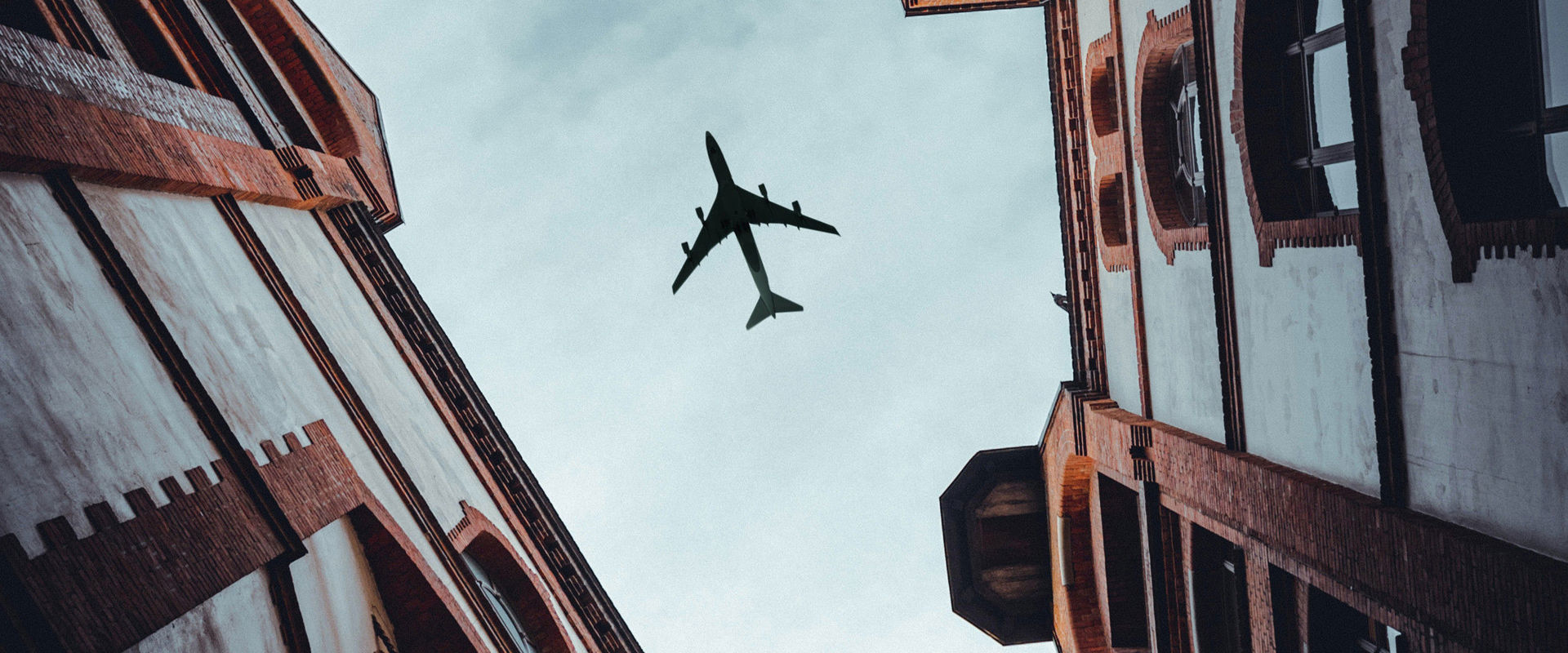 Foto eines Flugzeugs von unten zwischen den Häusern einer Stadtgasse.