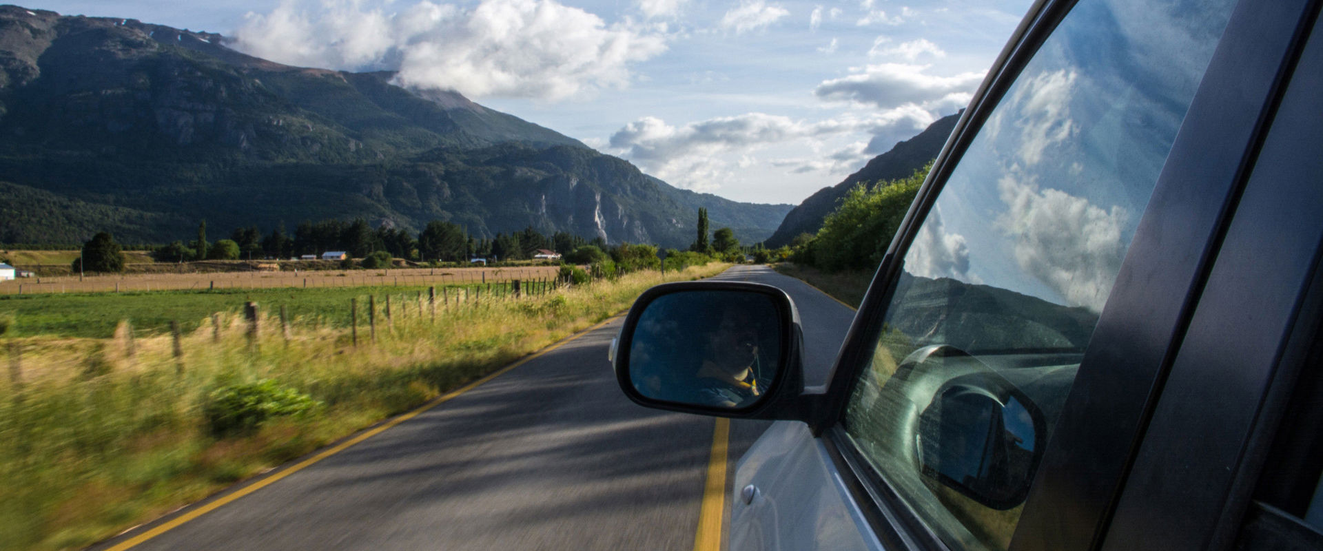 Fahrendes Auto auf einer Geraden. Foto vom linken hinteren Autofenster hinaus auf die Fahrerseite, die gerade Straße und die Umgebung.