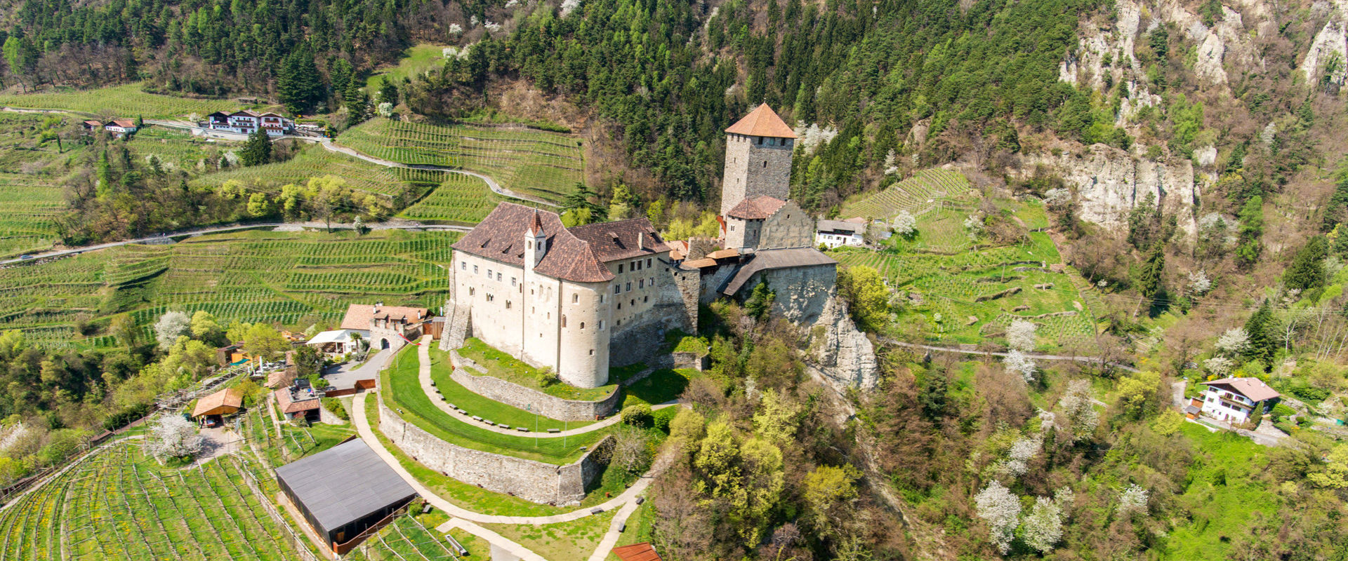 Schloss Tirol  Schloss Tirol von oben gesehen und umgeben von Wiesen, Bäumen, Weinreben und Häusern.