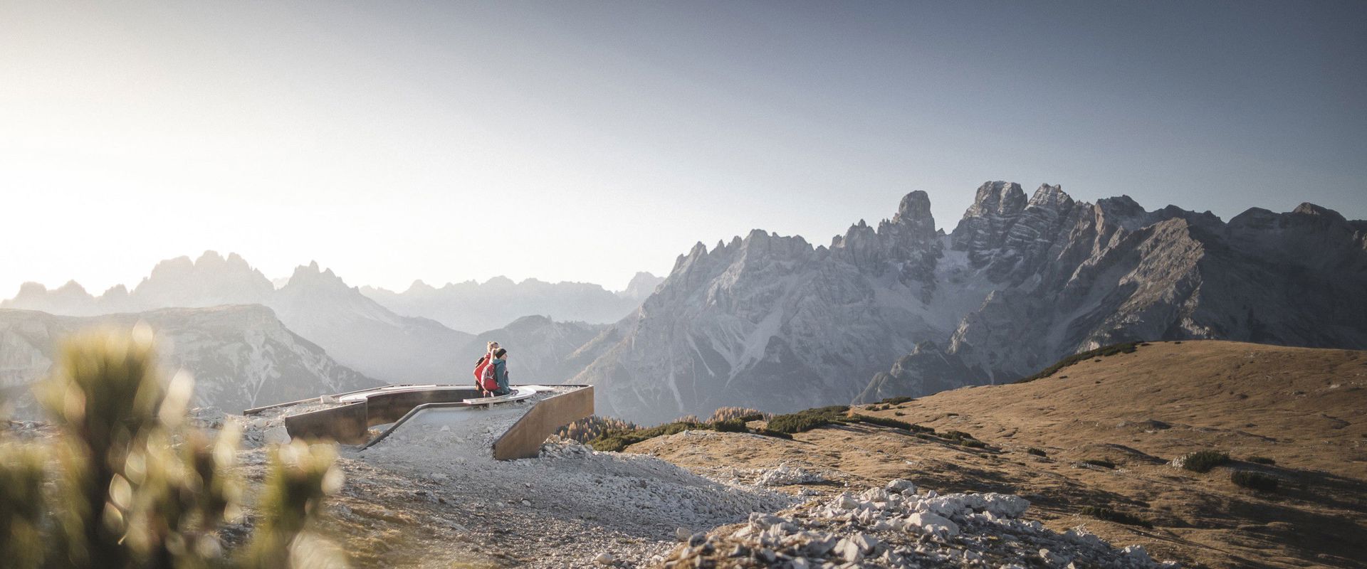 Paar sitzt an einem Aussichtspunkt und blickt auf die kahlen Felsen der Dolomiten.