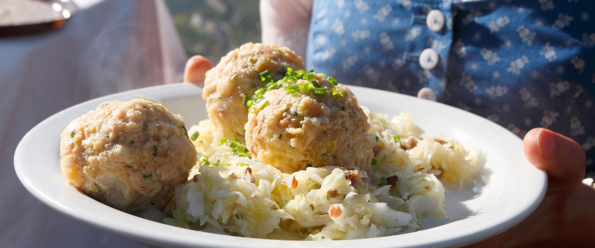Knödel Kellnerin serviert 3 Knödel mit Krautsalat.