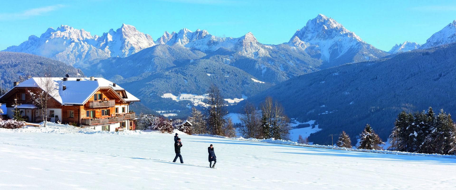 Winterspaziergänge Eine 3-köpfige Familie spaziert auf der frisch beschneiten Wiese.