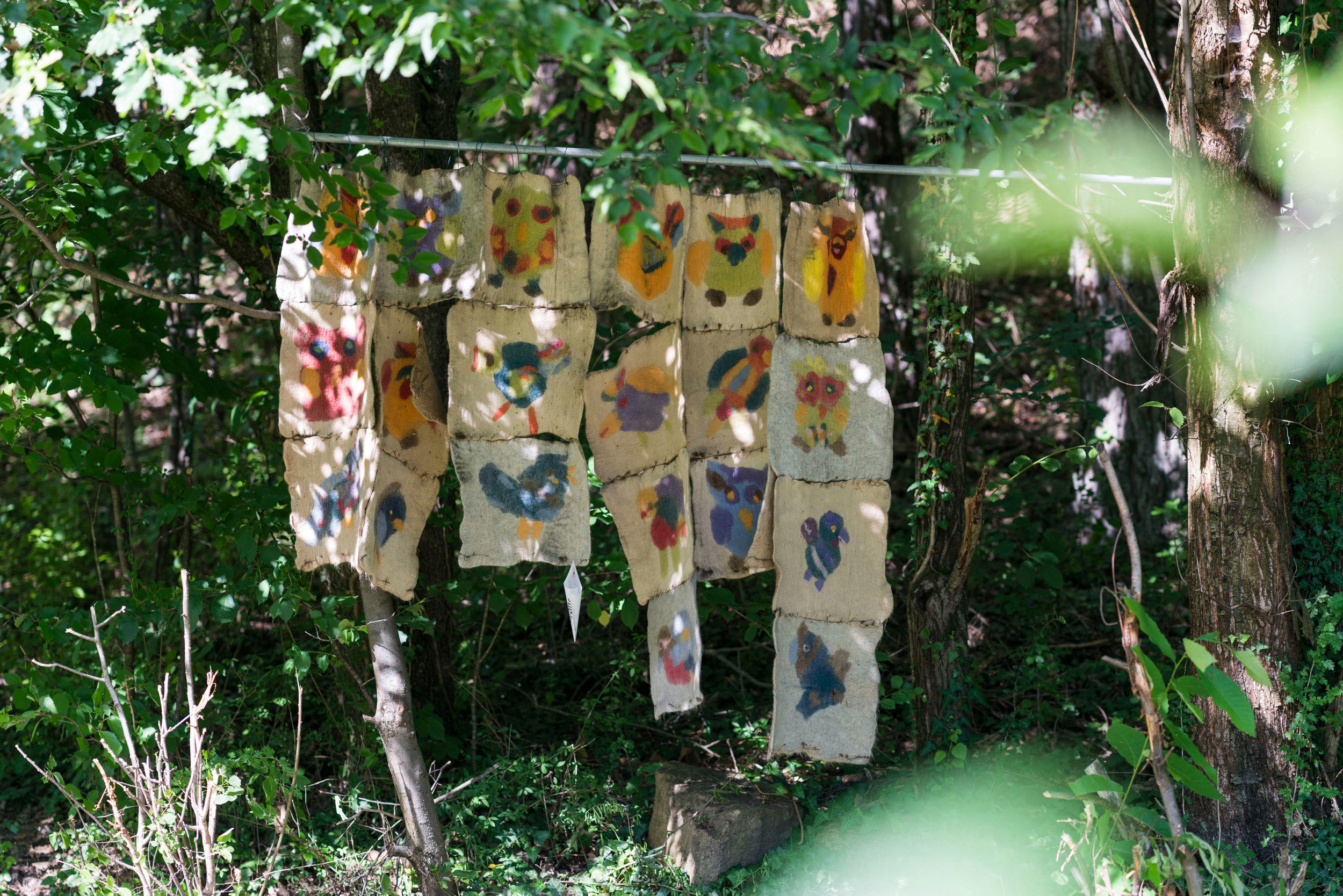 Filzfiguren hängen an einem Stab zwischen den Bäumen im Wald.