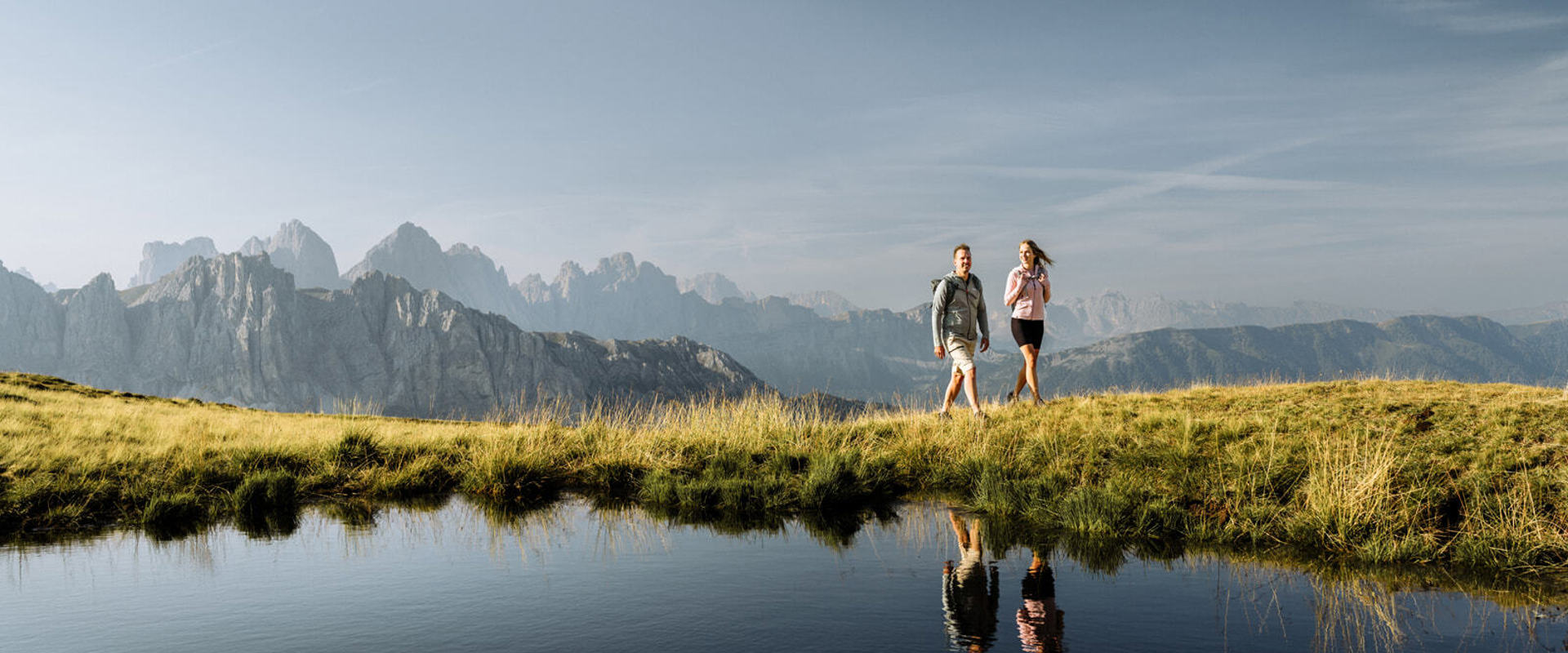 Wanderer spiegeln sich in Bergsee mit Berggipfeln im Hintergrund
