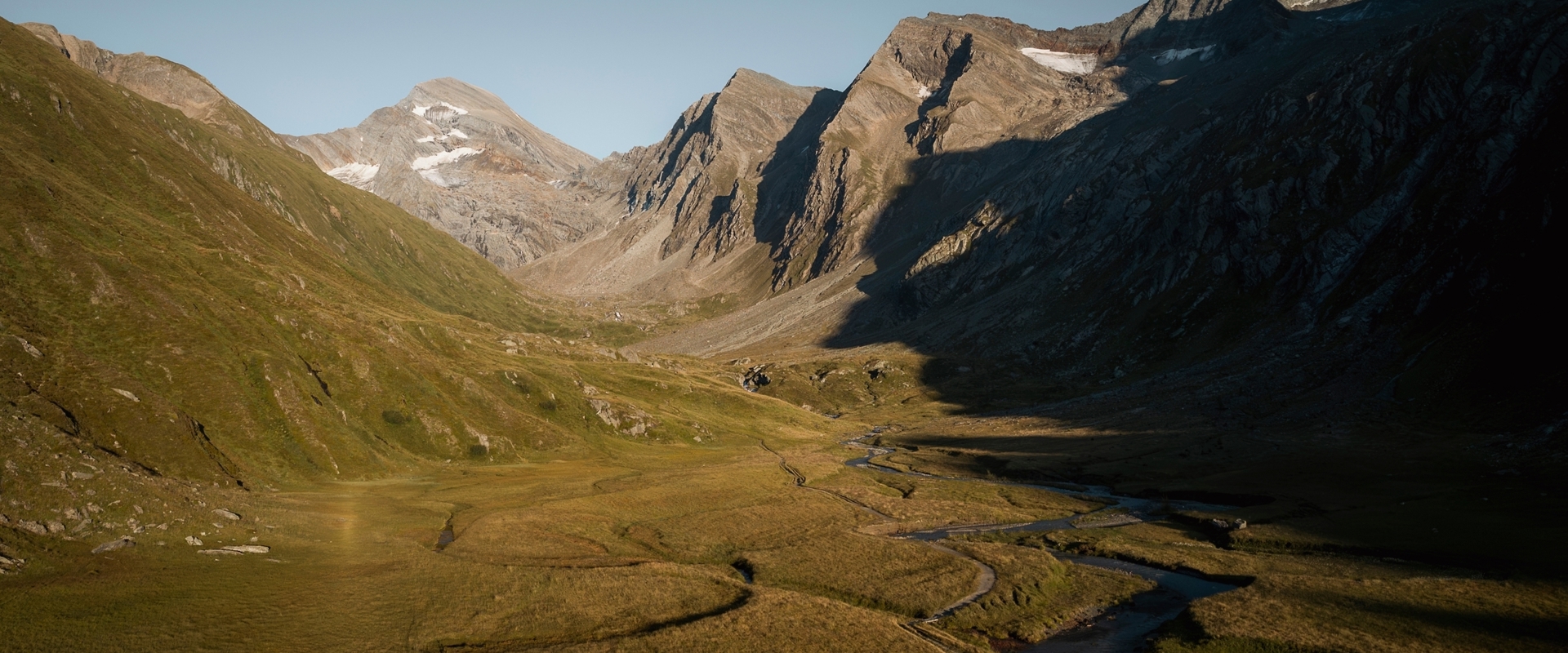Sich schlängelnder Fluss in Hochmoor mit Bergspitzen im Abendlicht