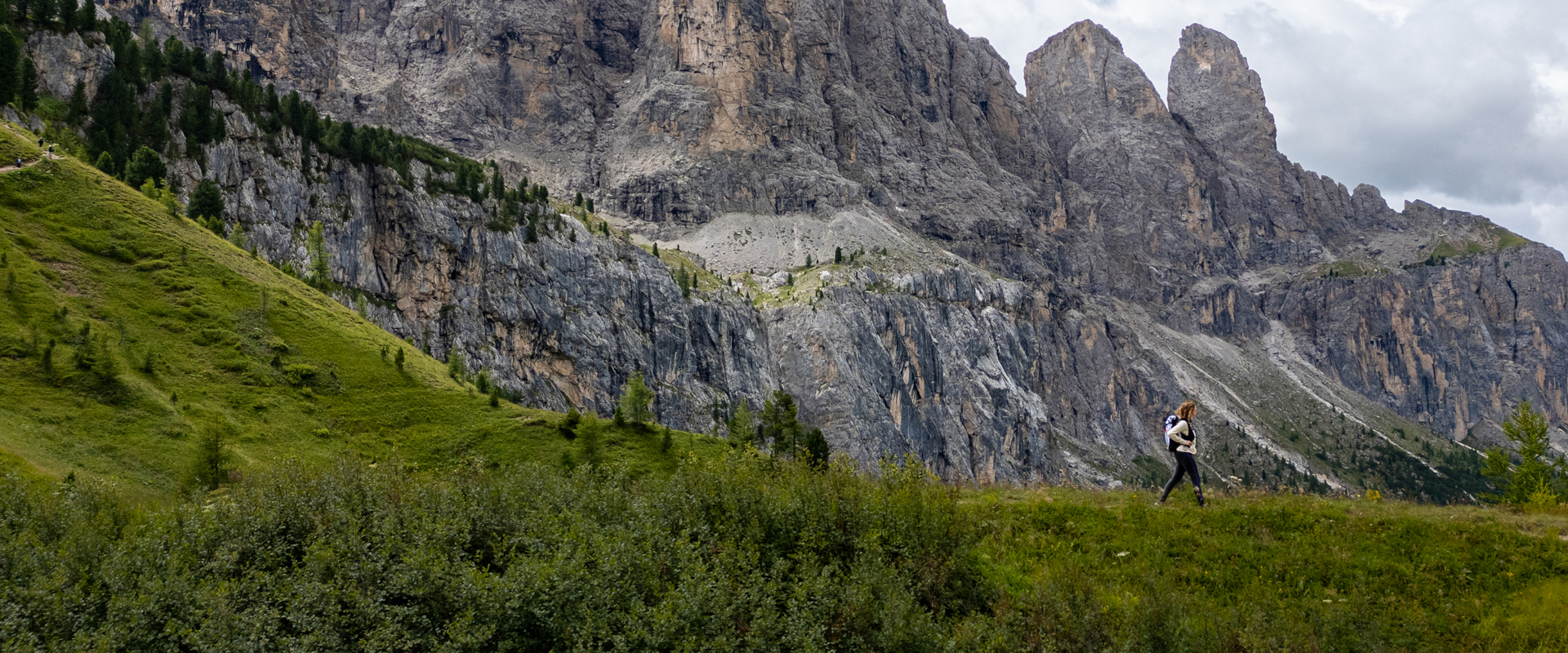 Grödner Joch Wanderer auf Bergwiese mit Felswänden im Hintergrund