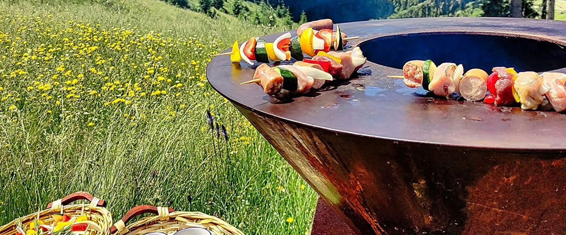 Grill steht mitten in der Wiese mit Spießchen drauf.