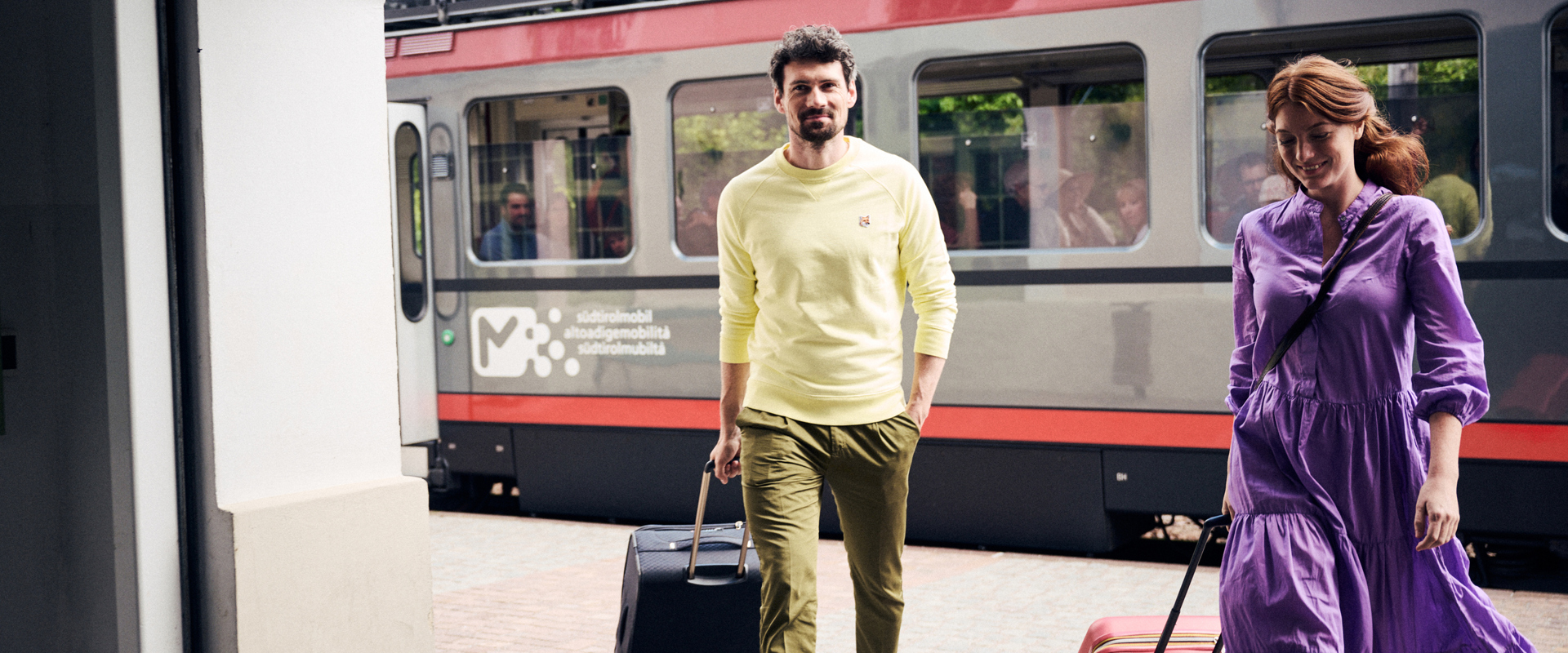 Zugfahren in Südtirol Paar mit Koffern am Bahnhof, mit Zug im Hintergrund