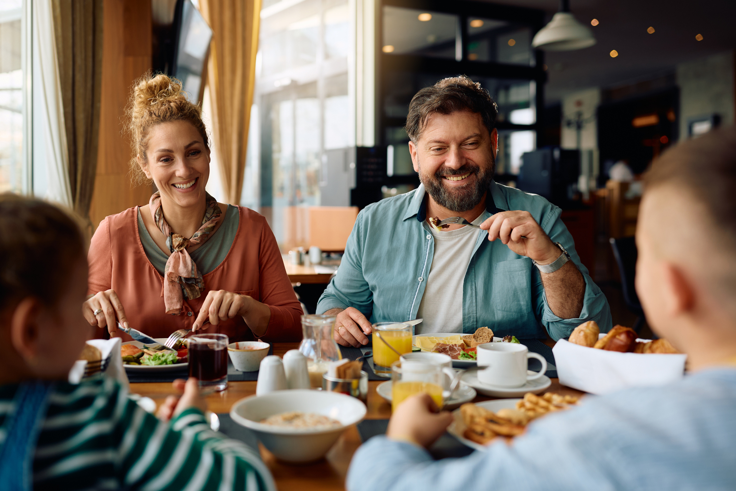 Familie sitzt im Hotel am Tisch, isst Frühstück mit Kaffee, Brot und Waffeln