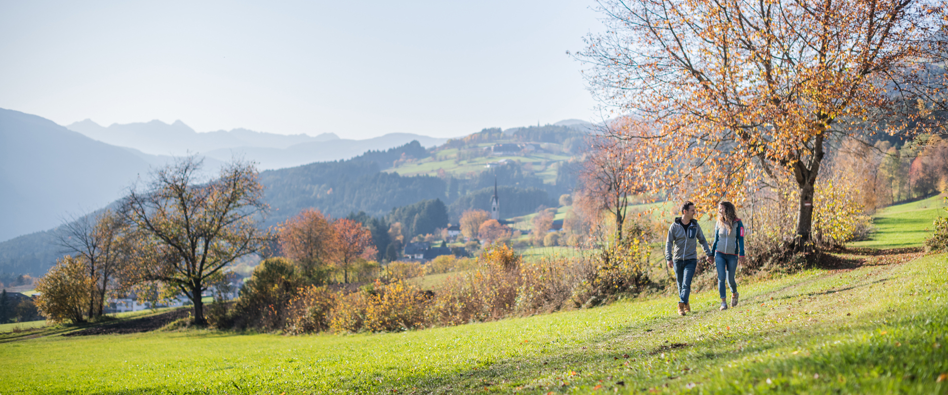 Eine Frau und ein Mann wandern durch die bunte gefärbte Herbstlandschaft oberhalb von Pfalzen bei Bruneck.