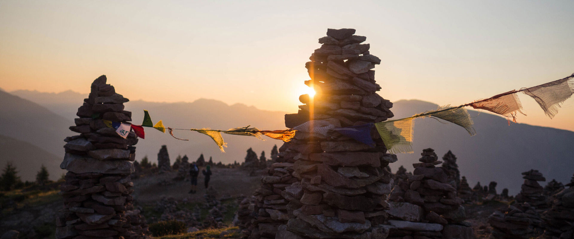 Stoanerne Mandln Stoanerne Mandln und Gebetsfahne am Berggipfel bei Sonnenaufgang oder -untergang.