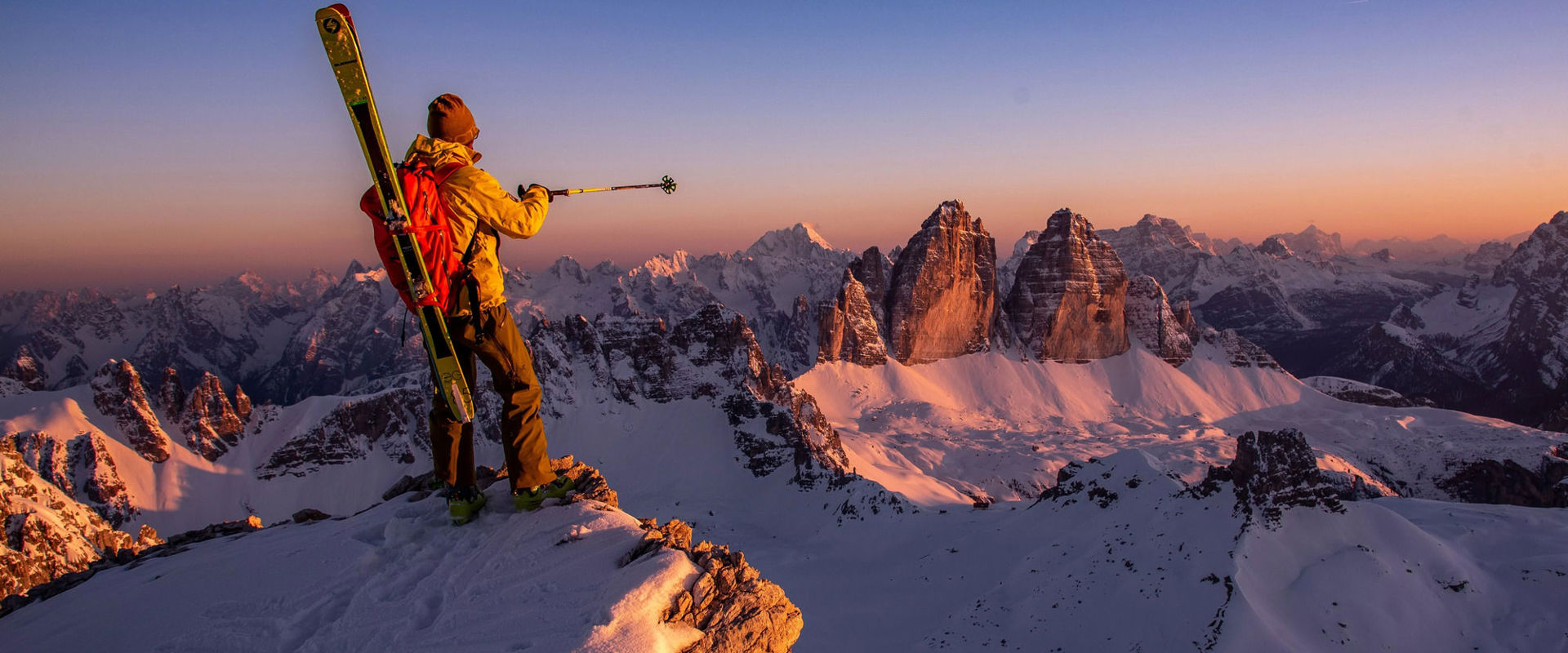 Alpinschule Drei Zinnen in Sexten Ein Skitourengeher bewundert die Drei Zinnen, nachdem er den Gipfel mit seinen Skiern auf den Schultern erklommen hat.