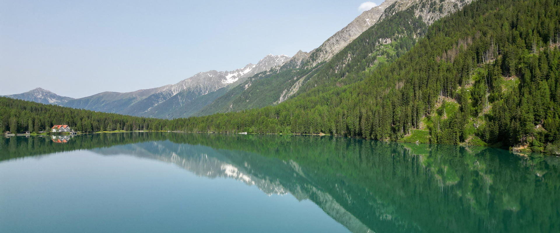 Grünblauer Bergsee (Antholzer See) umgeben von dichtem Wald