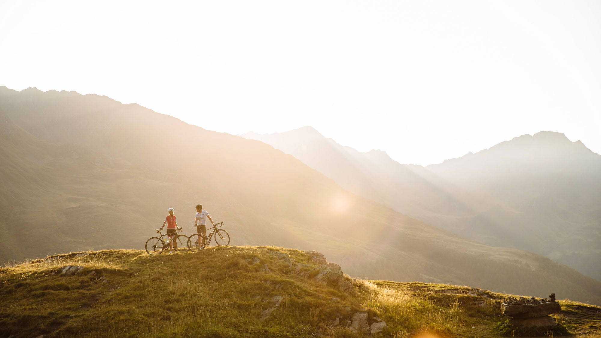 Zwei Radfahrer stehen mit den Fahrrädern am Berg und genießen die Morgensonne.