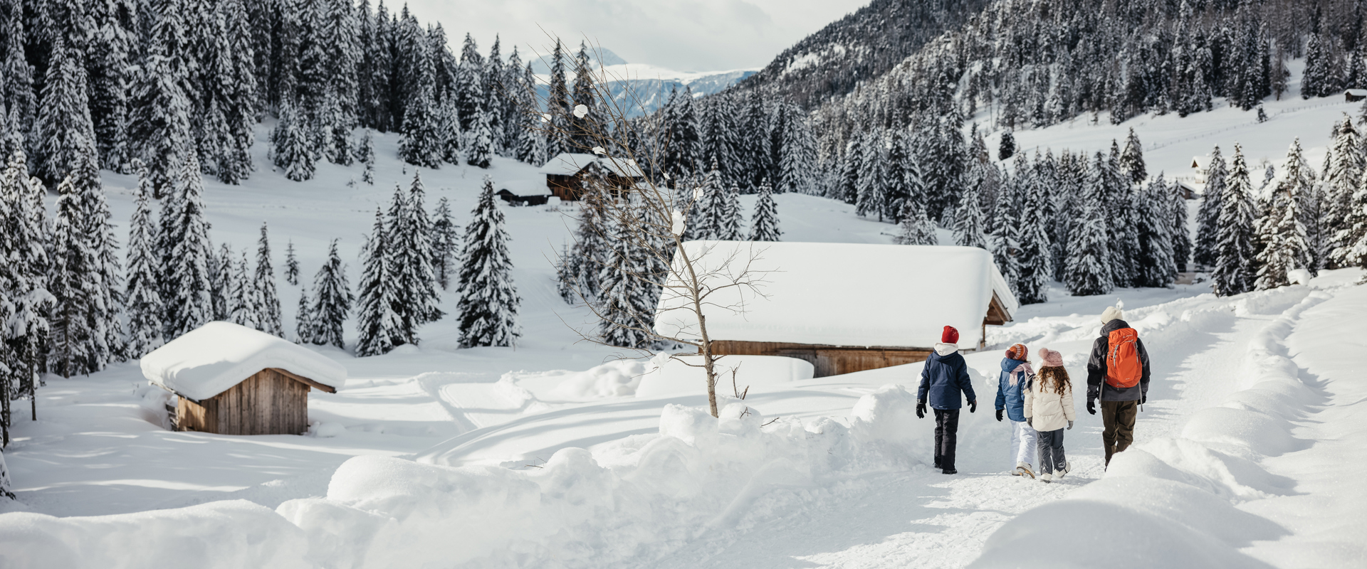 Winterwandern Familie wandert auf Winterwanderweg durch Schneelandschaft mit Berghütten.