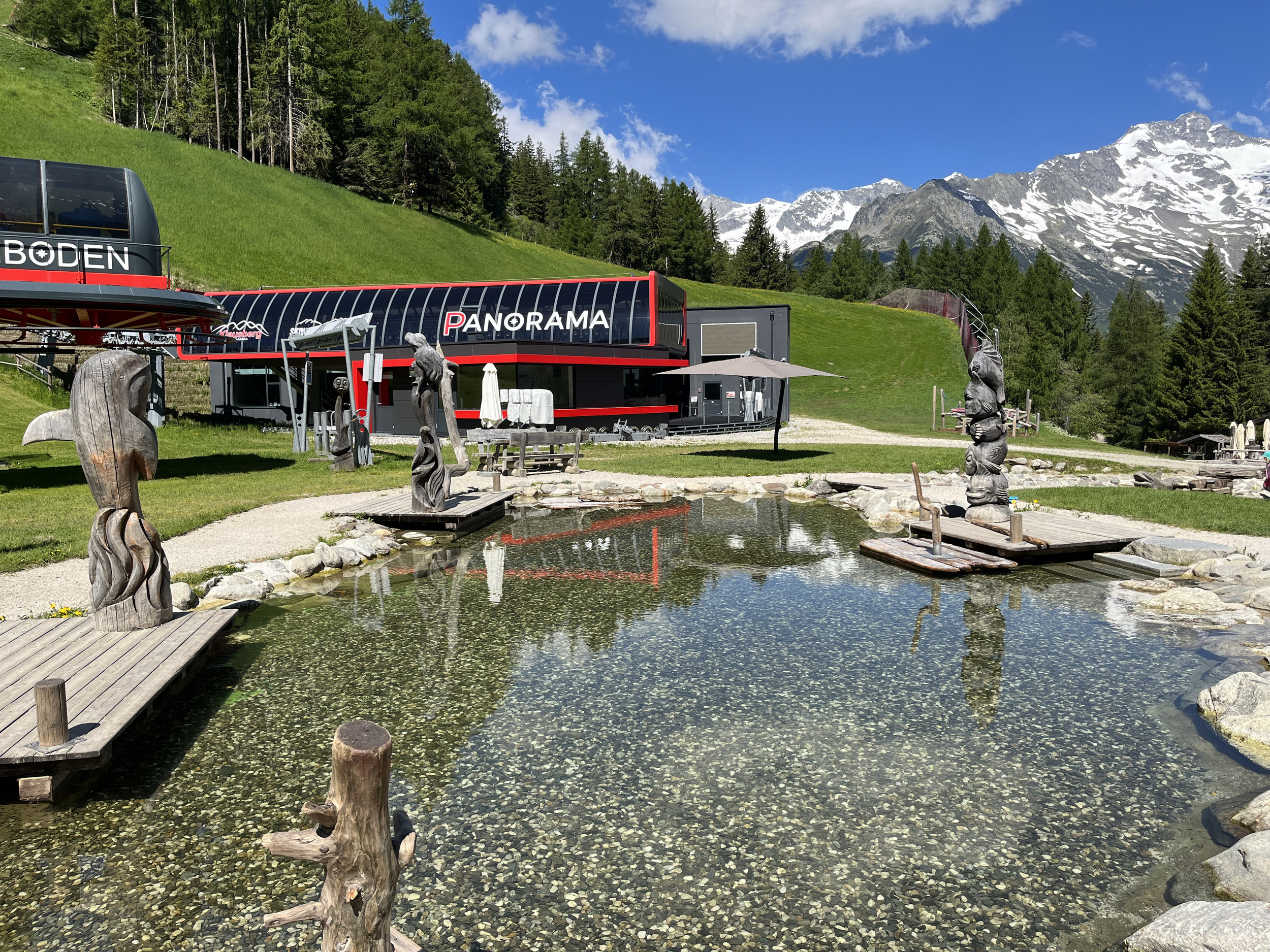 Seilbahnstation mit Teich und geschnitzten Figuren