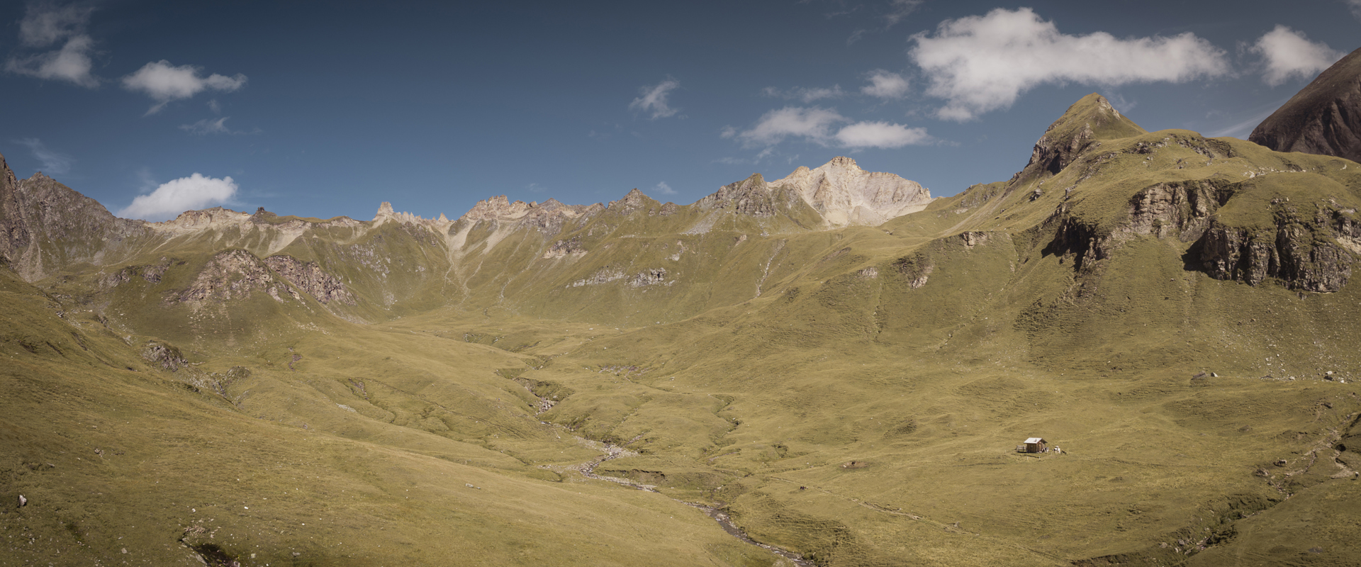 Sanfte Bergwiesen, Hütte und Bergspitzen am Horizont
