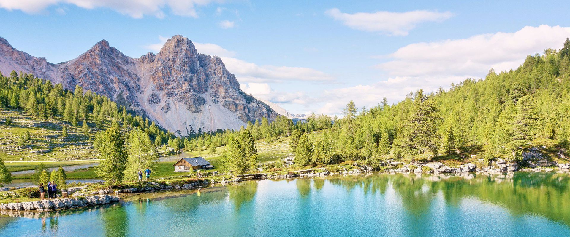 Naturpark Fanes-Sennes-Prags Türkisblauer See umgeben von grünen Wiese und Bäumen, mit Blick auf die Dolomiten.